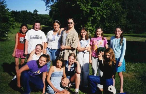 A group of girls and counselors posing outdoors in summer.