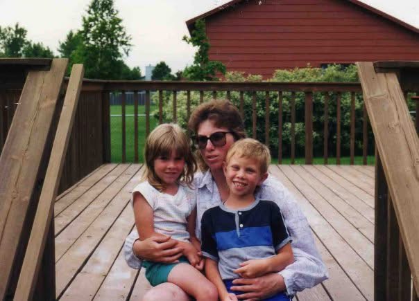 A young April with her mother and brother on a wooden deck.