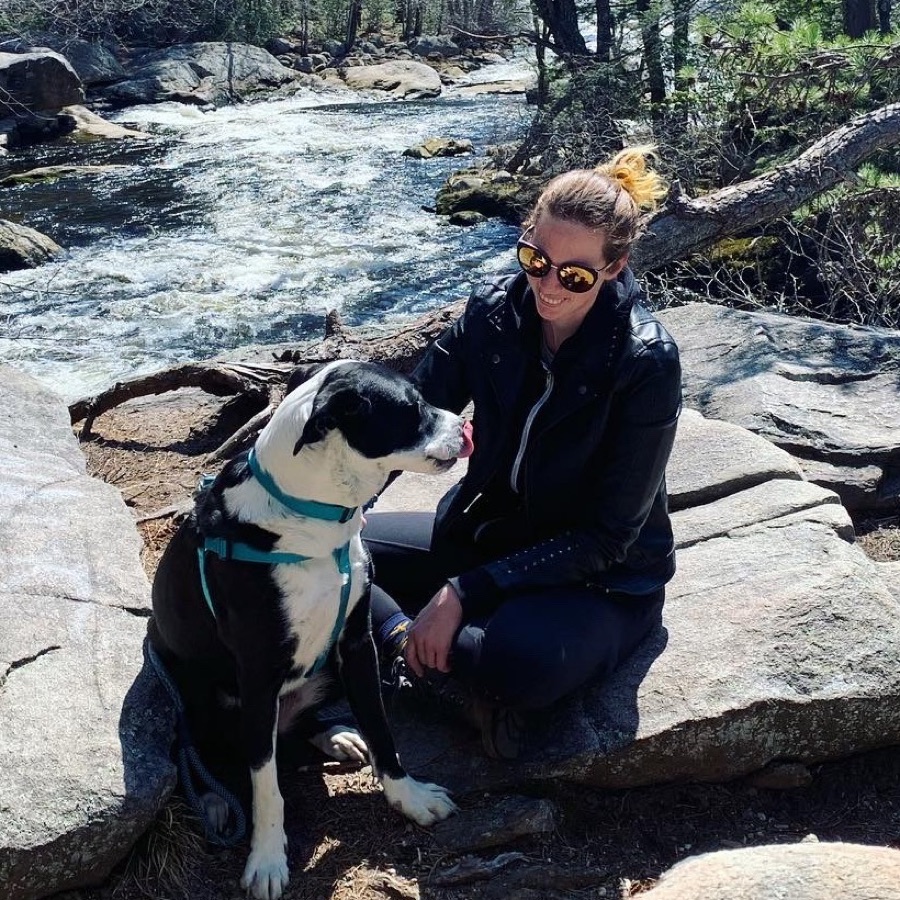 April sitting on river rocks with her black and white dog